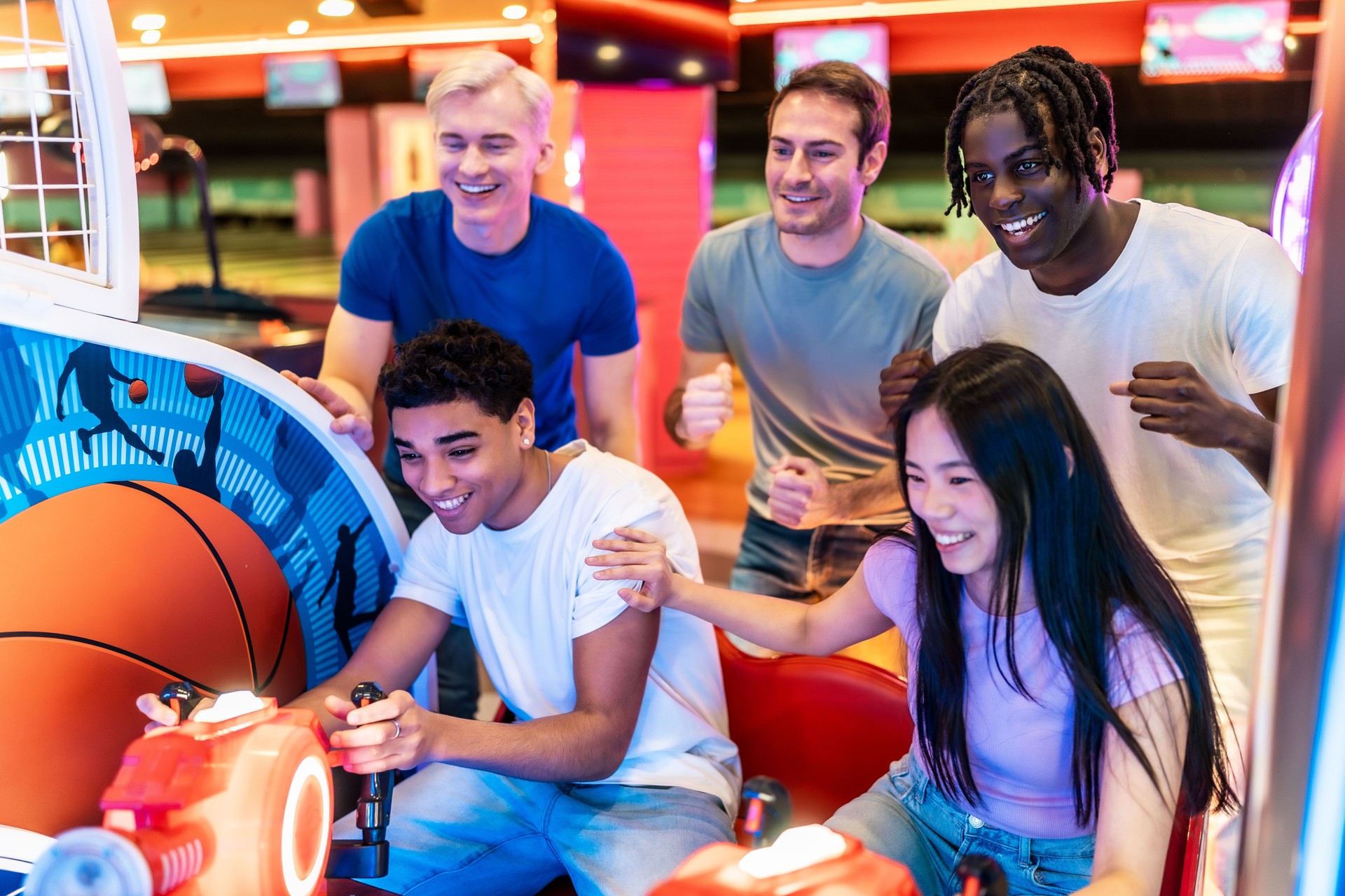 Young multiethnic friends playing arcade basketball game together